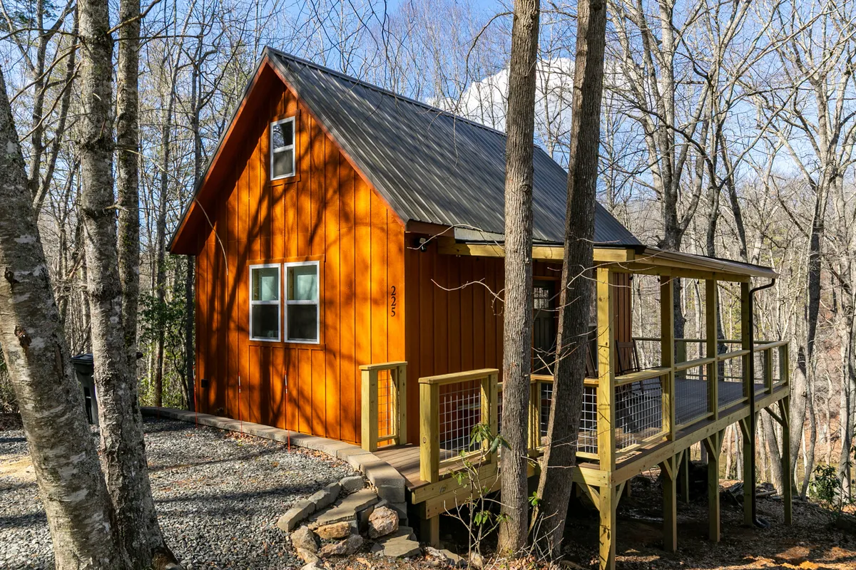A bright orange exterior cabin with large windows and a spacious deck area, nestled among trees. The deck is an inviting space for relaxing, outdoor dining, and enjoying the surrounding natural environment.