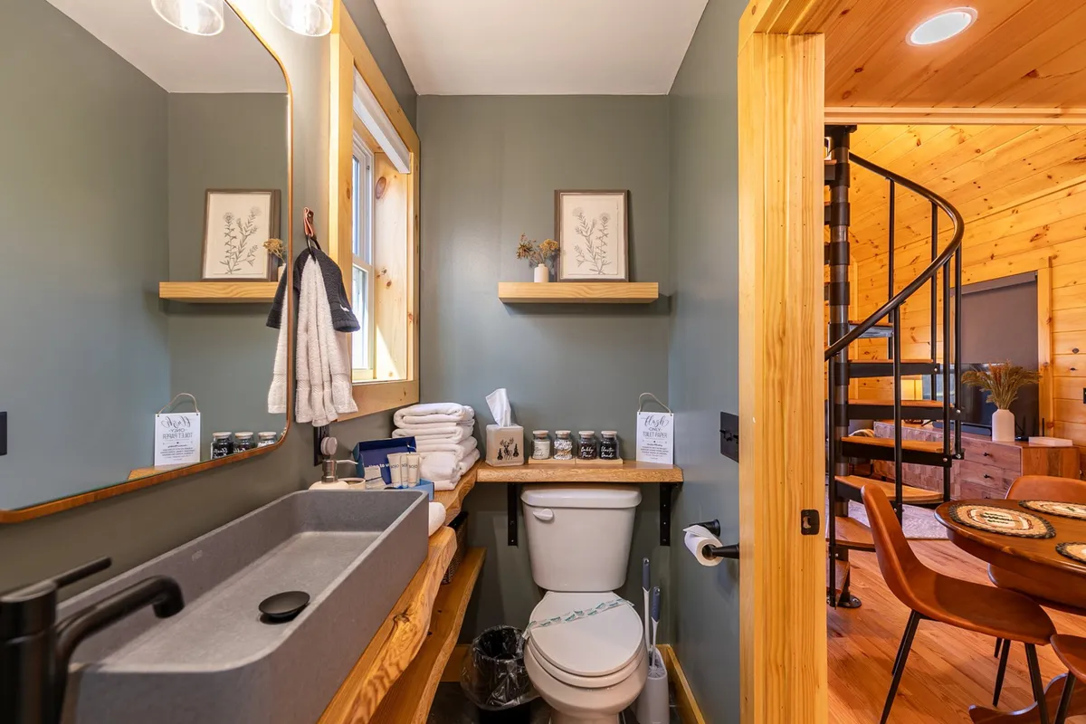 A tranquil bathroom vignette featuring a vintage-style mirror, sleek gray sink, and wooden shelves adorned with subtle decor. The overall mood is serene and composed, highlighting the bathroom's relaxing qualities and attention to detail.