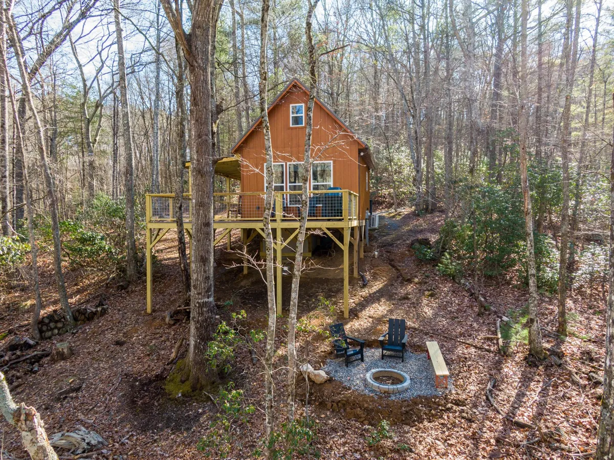 A wide-angle view of the cabin’s exterior, featuring the inviting wooden deck, the fire pit area surrounded by seating, and lush green space stretching into the trees. The image captures both the deck’s proximity to nature and the cozy atmosphere perfect for evening gatherings and stargazing.