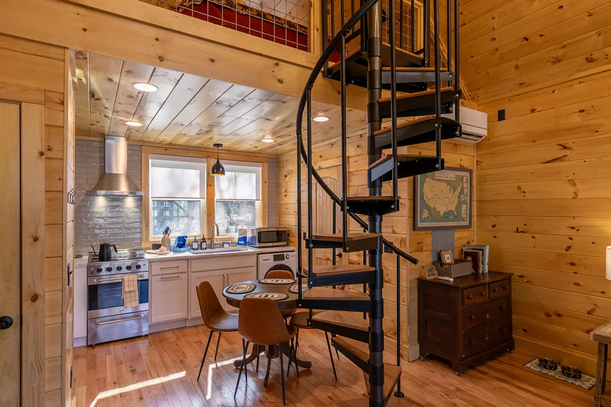 This inviting interior shot features a prominent spiral staircase rising beside a cozy kitchen island and a welcoming dining table. The warm lighting and stylish furnishings invite guests to imagine relaxing evenings and shared meals in a space designed for comfort and togetherness.