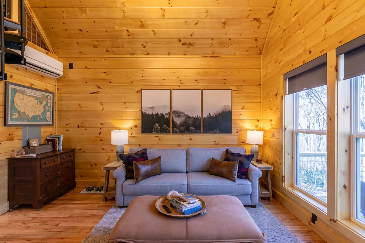 A warm, welcoming living area with a comfortable sofa, coffee table, and large windows that let in natural light. The windows frame views of the outdoors, suggesting a connection to nature and inviting relaxation after a day of exploration.